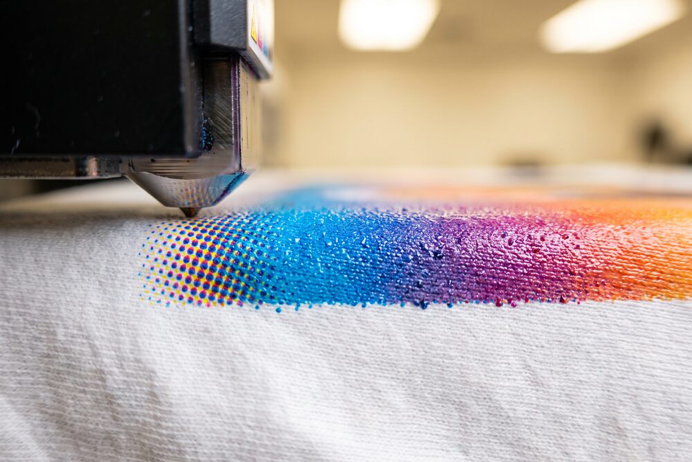 A digital printhead laying a full-colour halftone gradient across a white tee