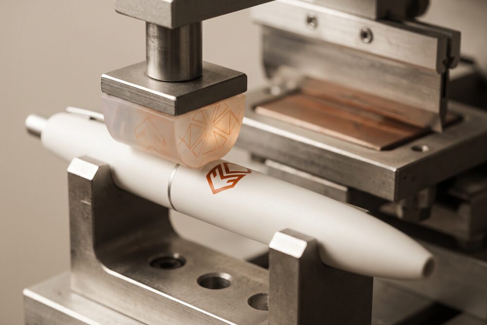 A silicone pad laying an orange mark onto the curved barrel of a pen